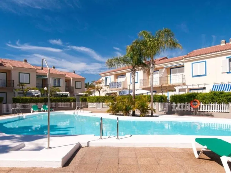 Holiday villa in the Canary Islands with a spacious outdoor pool, sun loungers, and palm-lined communal gardens.