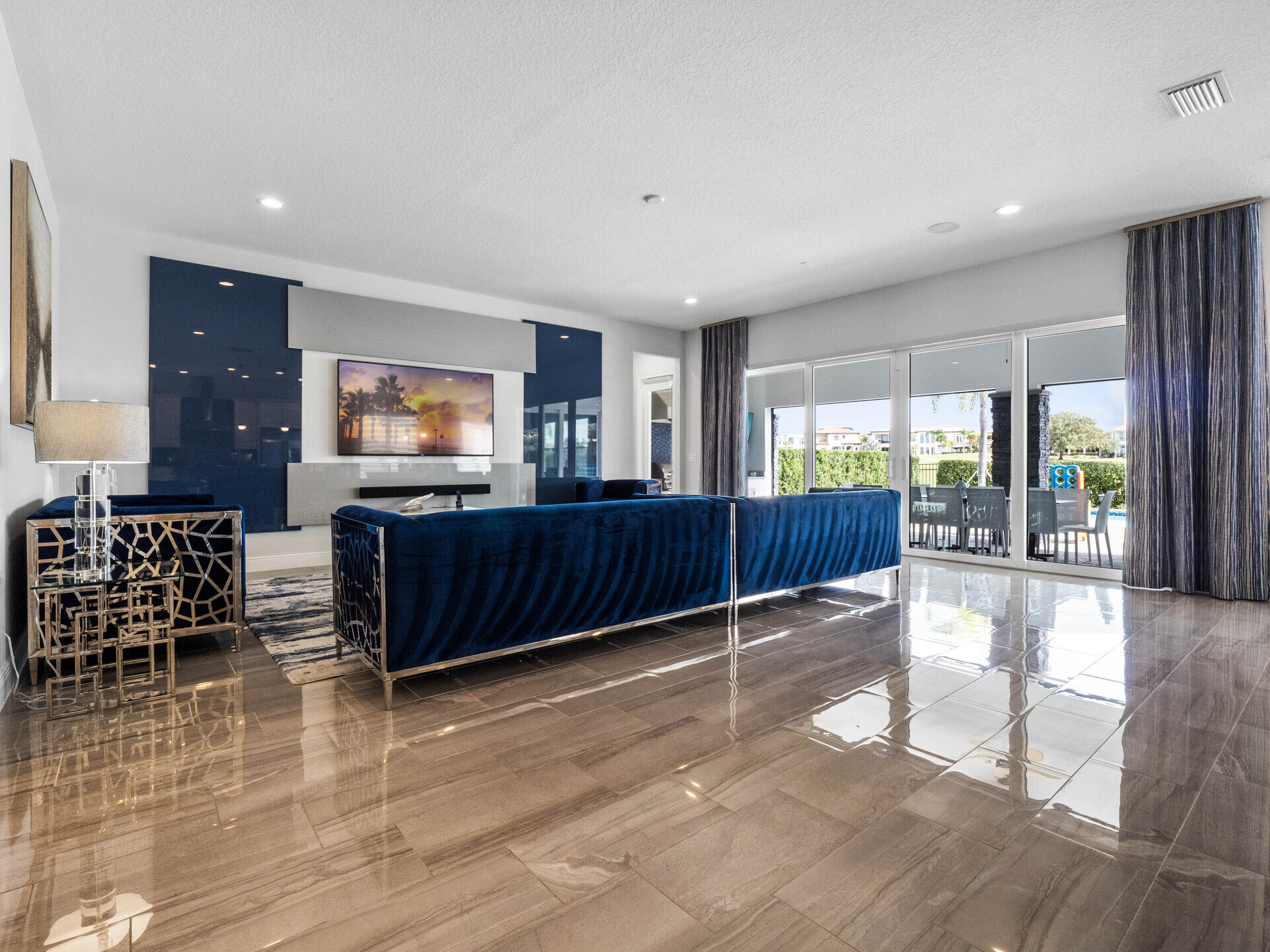 Enter our living room, adorned in calming shades of blue, with a glass door inviting you to the patio and pool area, flooding the space with natural light and promising serene moments of relaxation.
